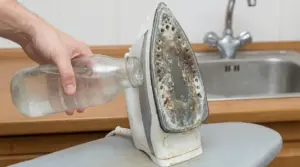 Mano versa acqua in un ferro da stiro con piastra incrostata di calcare vicino al lavandino