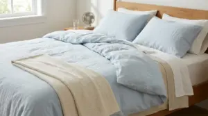 Letto con lenzuola chiare e copriletto leggero, con piccolo ventilatore sul comodino per dormire al fresco