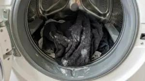 Panni scuri nel cestello della lavatrice con residui bianchi di detersivo, causa di bucato duro