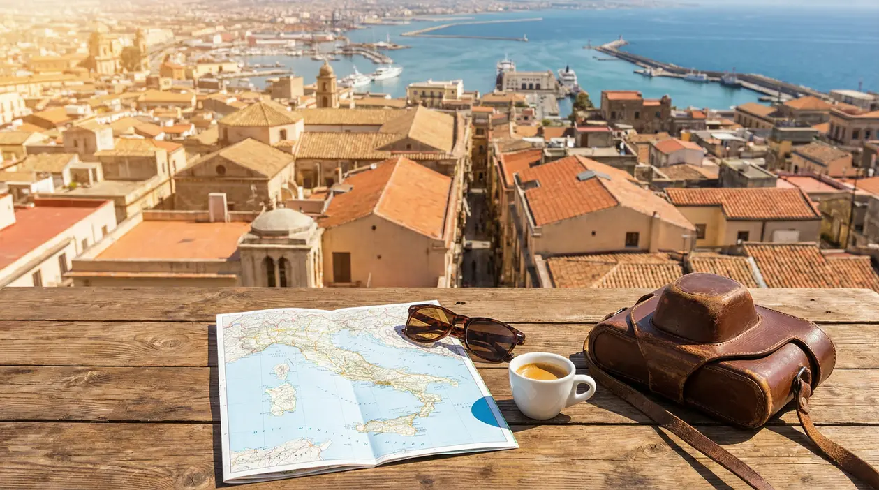 Vista panoramica di una città costiera italiana con mappa, caffè e macchina fotografica su un tavolo