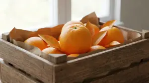 Cassetta di legno con arance fresche adagiate su carta, conservate a temperatura ambiente vicino a una finestra