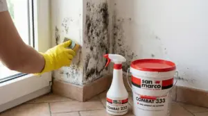 Persona con guanti gialli pulisce muffa nera su una parete vicino a una finestra con spugna e detergente