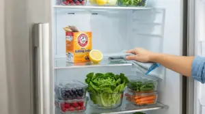 Mano che pulisce il ripiano del frigorifero con panno, limone e bicarbonato per eliminare i cattivi odori