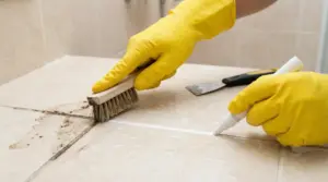 Mani con guanti gialli puliscono e ravvivano le fughe delle piastrelle con spazzola e penna sbiancante