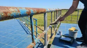 Persona che rimuove la ruggine da una ringhiera metallica esterna con una spazzola prima della verniciatura