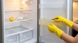 Pulizia del frigorifero con spugna su un cassetto ingiallito, accanto a limone e bicarbonato