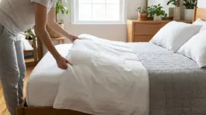 Persona che sistema il letto al mattino in una camera luminosa con lenzuola bianche