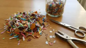 Coriandoli fai da te con ritagli di carta e foglie secche su un tavolo, accanto a forbici e perforatrice