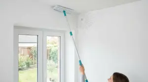 Persona che rimuove una ragnatela da un angolo del soffitto con un mocio telescopico
