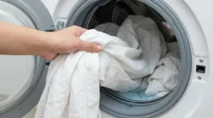 Una mano inserisce lenzuola bianche nella lavatrice per un lavaggio efficace contro acari e batteri