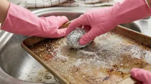 Mani con guanti rosa puliscono una teglia sporca con una pallina di foglio di alluminio e sale nel lavello