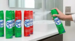 Mano che spruzza spray disinfettante su una maniglia della porta, con bombolette su un piano del bagno