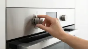 Mano che gira la manopola delle funzioni di un forno da incasso in acciaio inox, con simboli di cottura sul pannello.