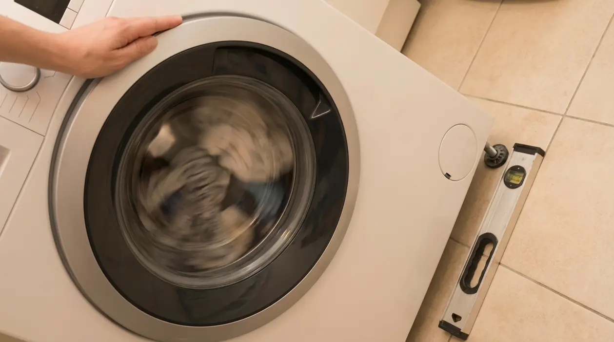 Persona che controlla il livello di una lavatrice mentre centrifuga, per ridurre vibrazioni e rumore