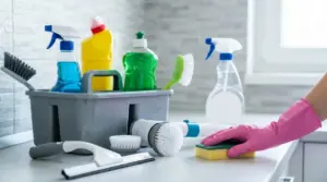 Prodotti e strumenti per la pulizia della casa su un piano cucina, con mano guantata che passa una spugna
