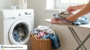 Persona piega indumenti su asse da stiro accanto a lavatrice e cesto della biancheria in casa