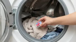 Mano che inserisce una pastiglia per lavastoviglie nel cestello della lavatrice con bucato e asciugamani