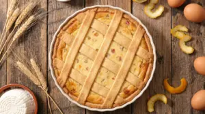 Pastiera napoletana in teglia con strisce di pasta frolla incrociate, su tavolo rustico con uova e scorze di agrumi