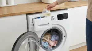 Persona versa detersivo liquido nel cassetto della lavatrice a carica frontale con bucato nel cestello