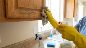 Persona con guanti gialli pulisce un pensile in legno in cucina con panno e spray detergente