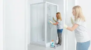 Persona che pulisce la cabina doccia con panno e detergente, per eliminare aloni e calcare