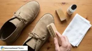 Spazzola che pulisce scarpe in camoscio beige su tavolo in legno con panno, gomma e detergente