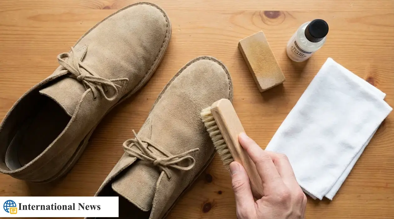 Spazzola che pulisce scarpe in camoscio beige su tavolo in legno con panno, gomma e detergente