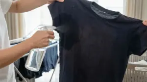 Persona spruzza una soluzione su una maglia nera per eliminare l’odore di sudore dalle ascelle