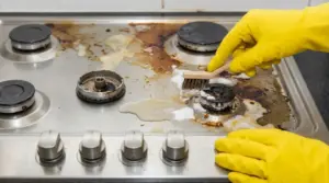 Pulizia di un fornello della cucina ostruito con spazzolina e detergente su piano cottura sporco