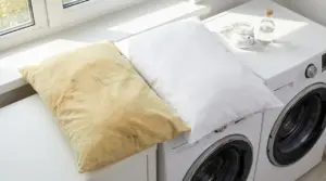 Due federe su lavatrice: una ingiallita e macchiata di sudore, l’altra bianca e pulita, accanto a barattolo e bottiglia
