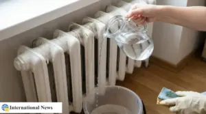 Mano che versa acqua da una brocca su un termosifone sporco, con secchio a terra per raccogliere lo sporco