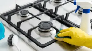 Pulizia dei bruciatori del piano cottura a gas con spugna e guanti, accanto a spray detergente